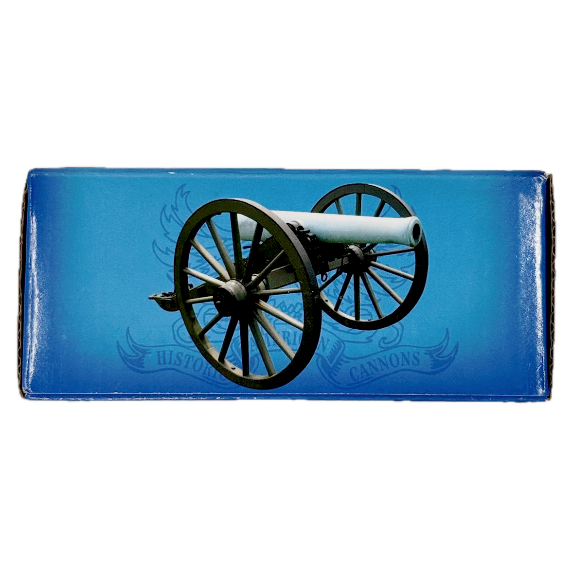 Cardboard box containing small brass replica Trail Cannon toy on a white background