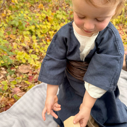 Child in blue colonial attire playing with wooden blocks with a natural background