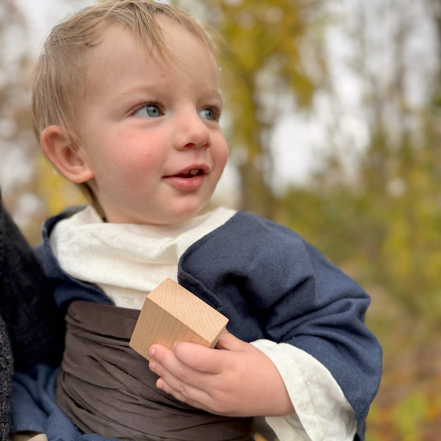 Child wearing colonial attire holding a wooden block outdoors with a blurred natural background