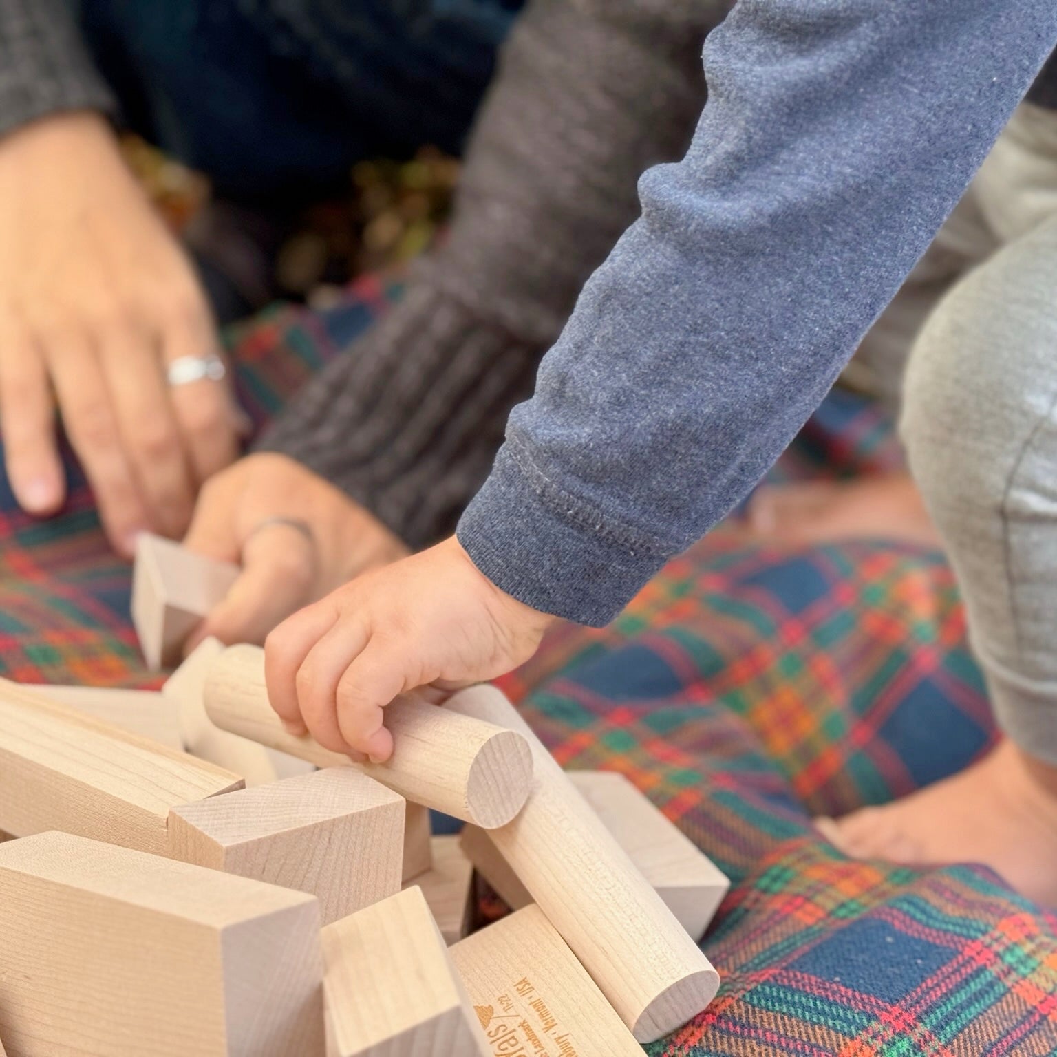Child playing with wooden blocks on a colorful plaid blanket