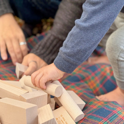 Child playing with wooden blocks on a colorful plaid blanket