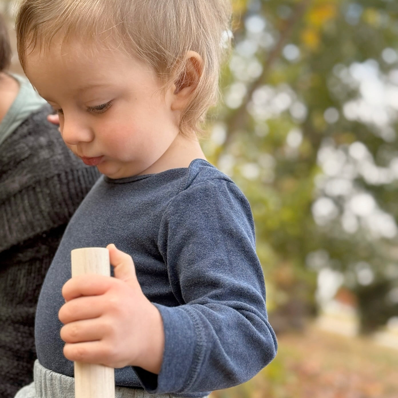 Child holding a wooden block outdoors with blurred greenery in the background