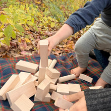 Child playing with wooden blocks on a plaid blanket outdoors in autumn.