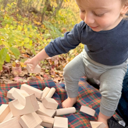 Child playing with wooden blocks outdoors on a colorful blanket