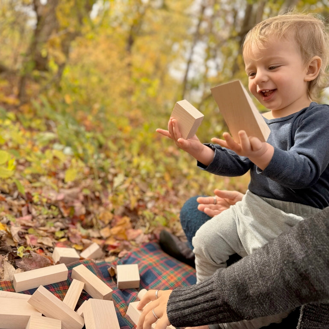Child playing with wooden blocks outdoors in a forest setting