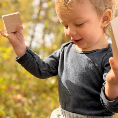 Child holding wooden blocks outdoors with a blurred natural background
