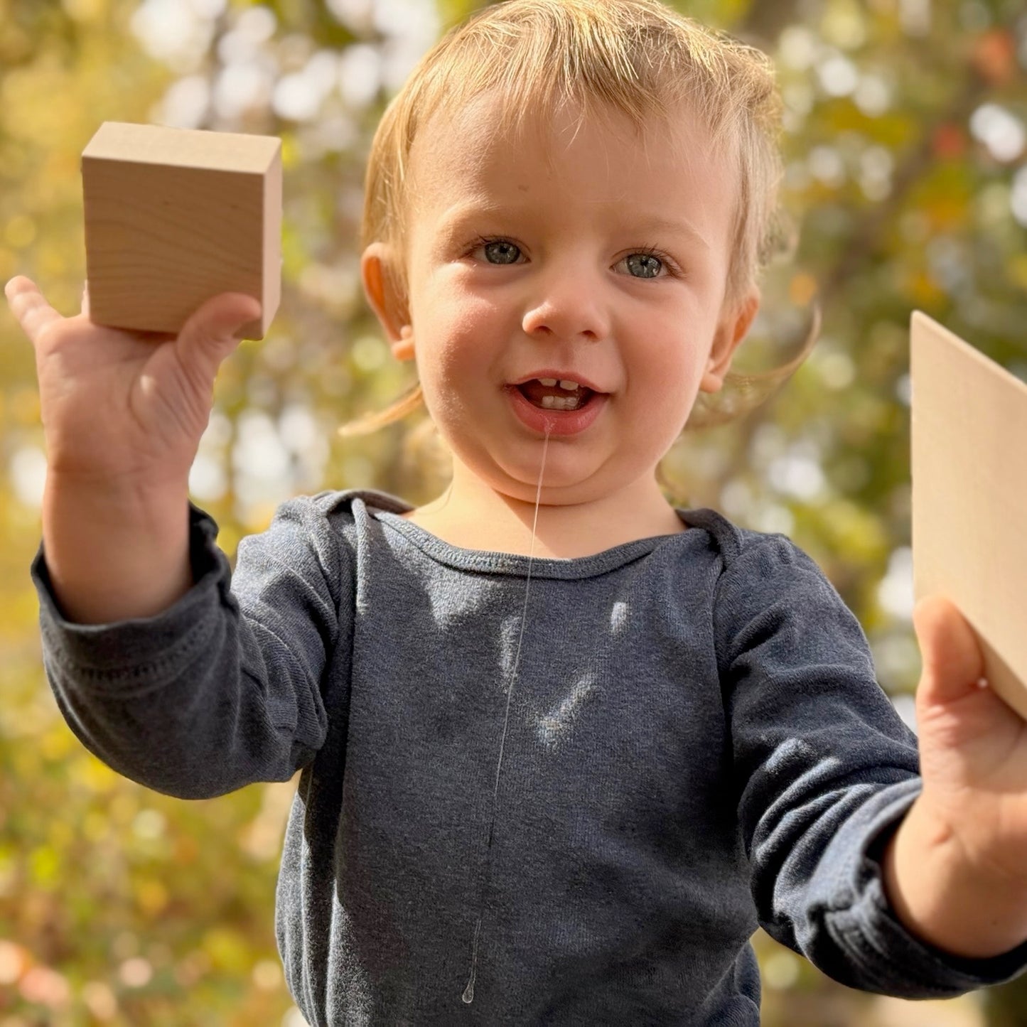 Child holding wooden blocks outdoors with a blurred natural background