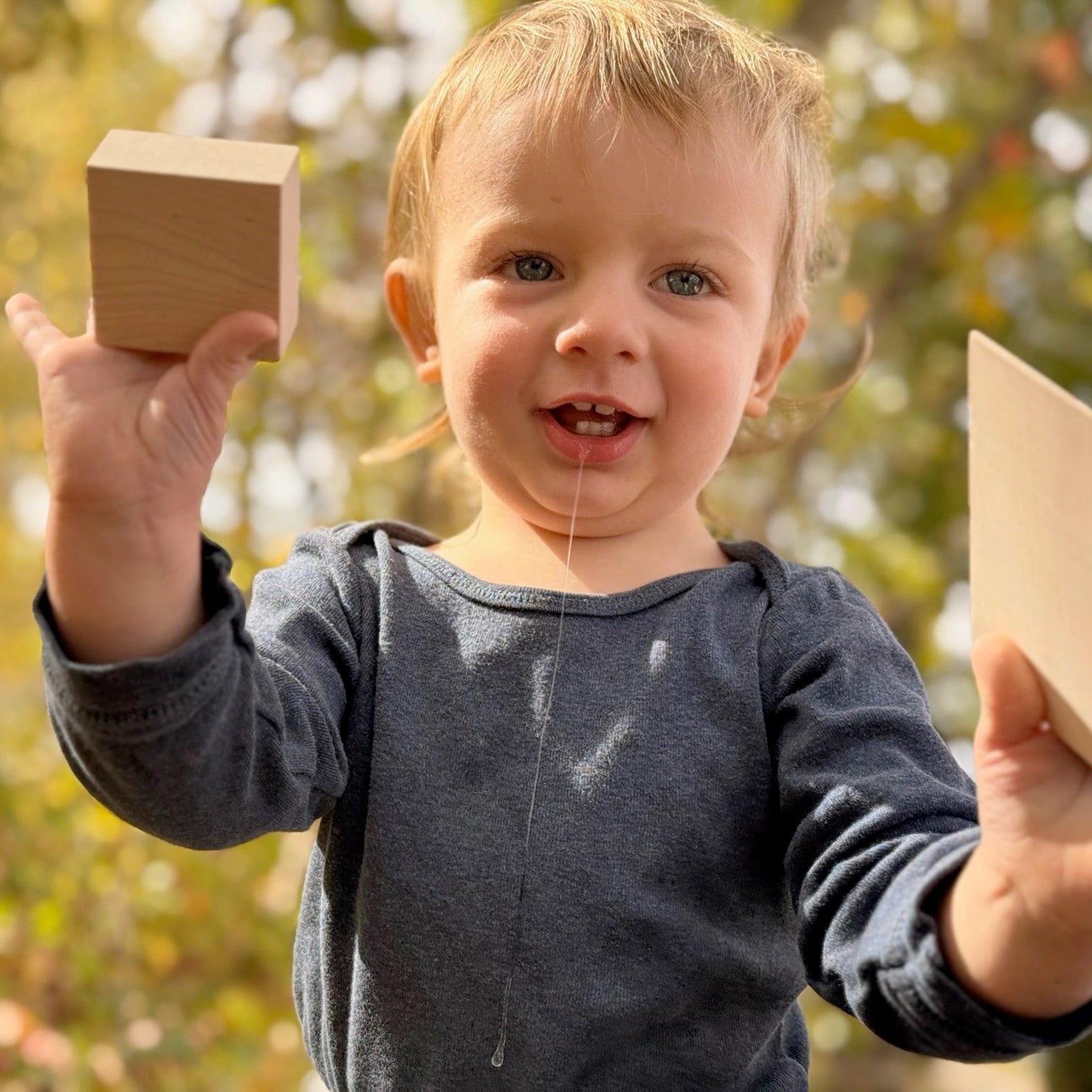 Child holding wooden blocks outdoors with a blurred natural background