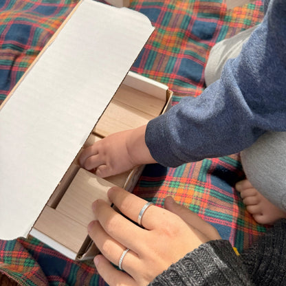 Two hands on a box of wooden building blocks against a plaid fabric background
