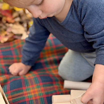 Child playing with wooden blocks on a colorful plaid blanket