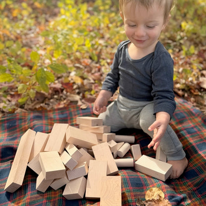 Child playing with wooden blocks outdoors on a plaid blanket