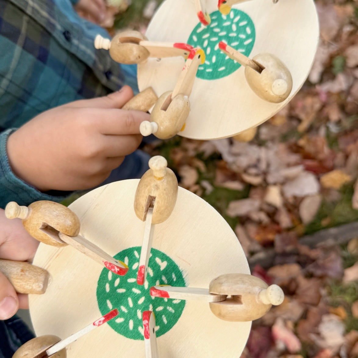 Two wooden Feeding Chickens toys being held by children against a blurred natural background.