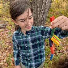 Child holding a colorful Jacob's Ladder toy in an outdoor setting with trees and leaves.