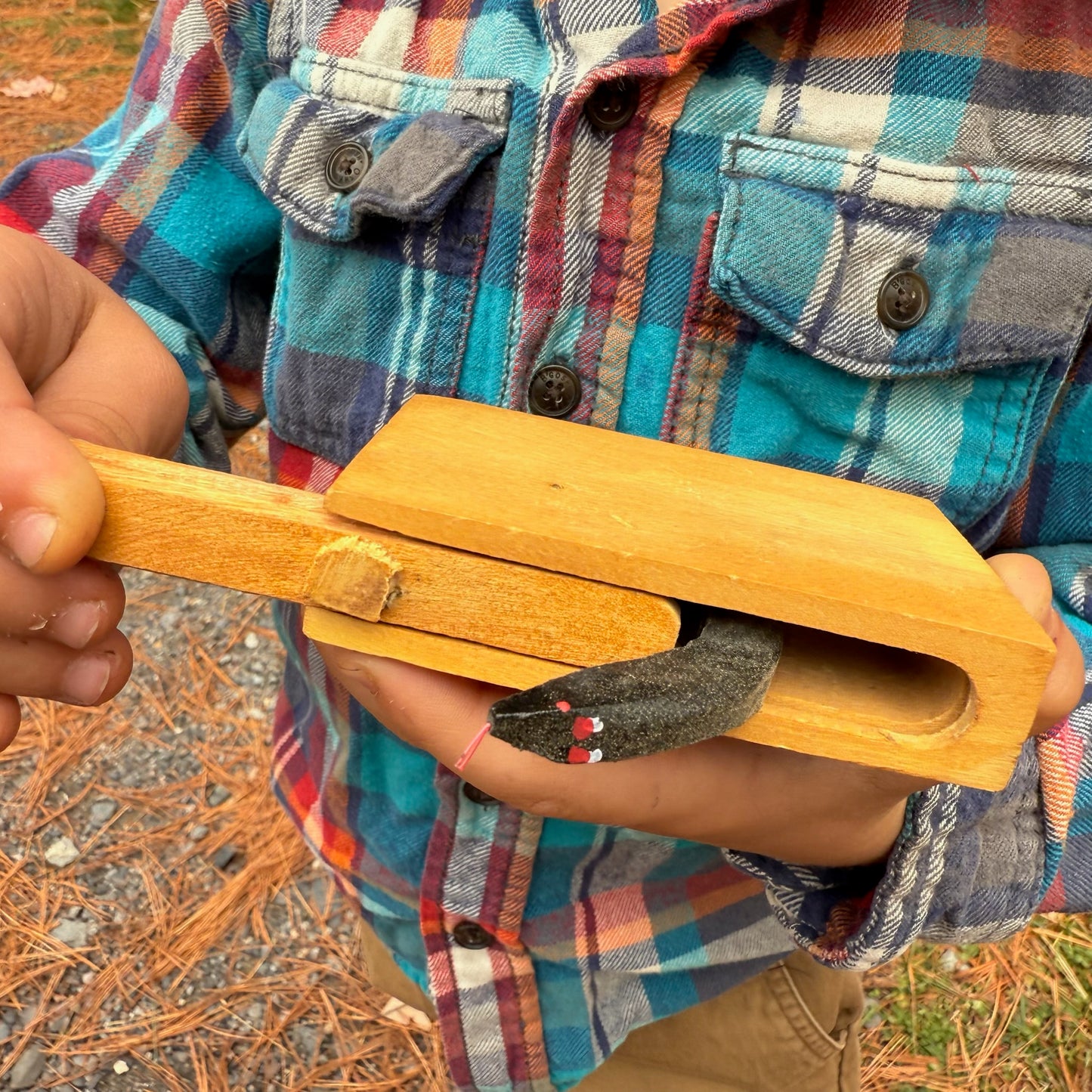 Child holding a Snake in the Box toy while wearing a plaid shirt outdoors