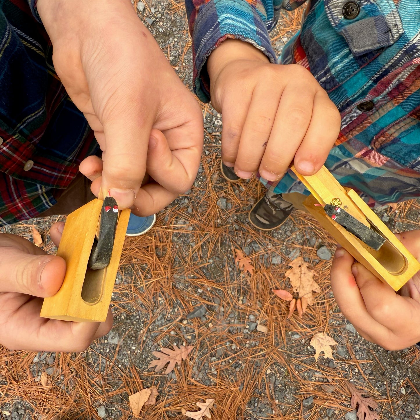 Children's hands holding wooden Snake in the Box toys on a ground with leaves