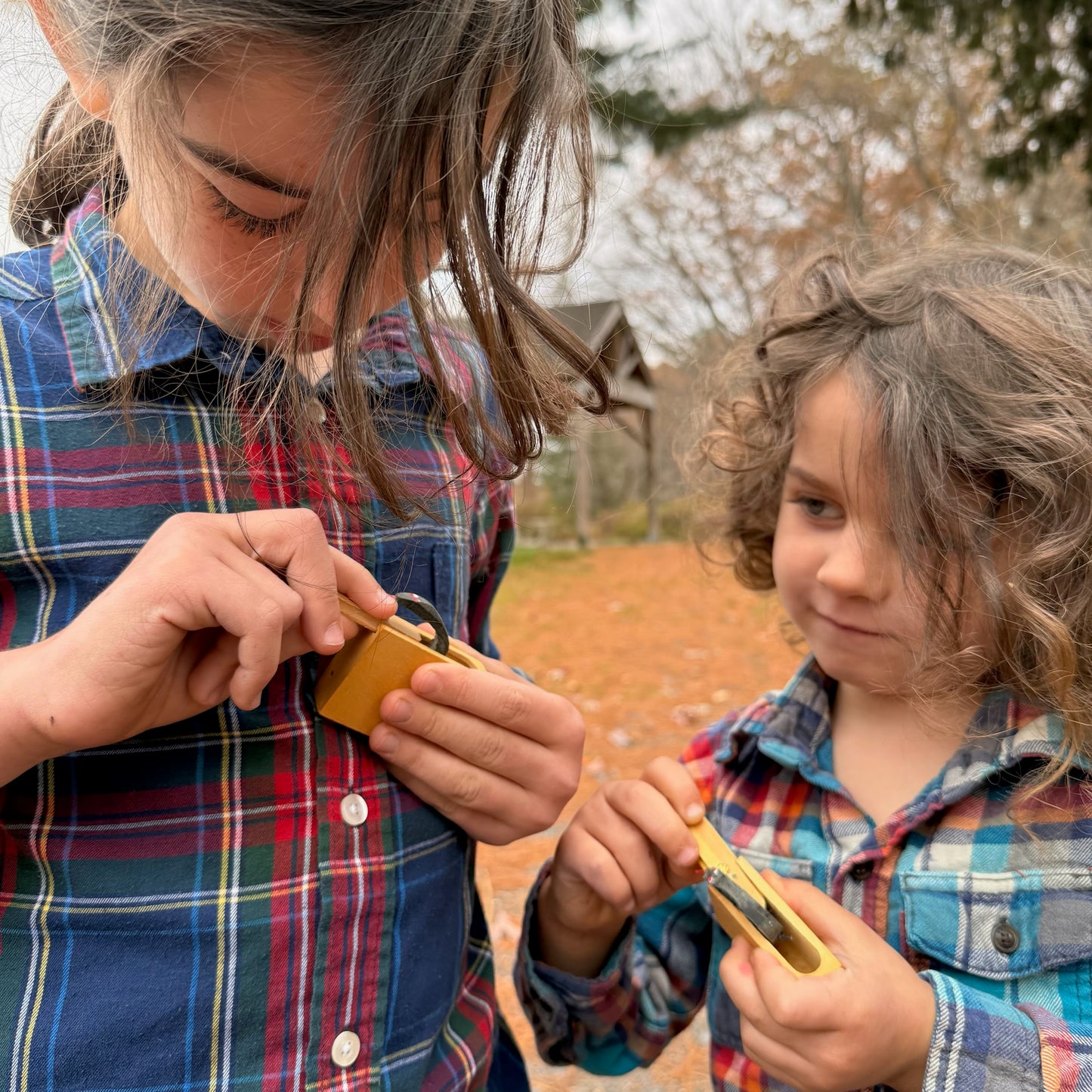 Two children in plaid shirts playing with small wooden Snake in the Box toys outdoors.