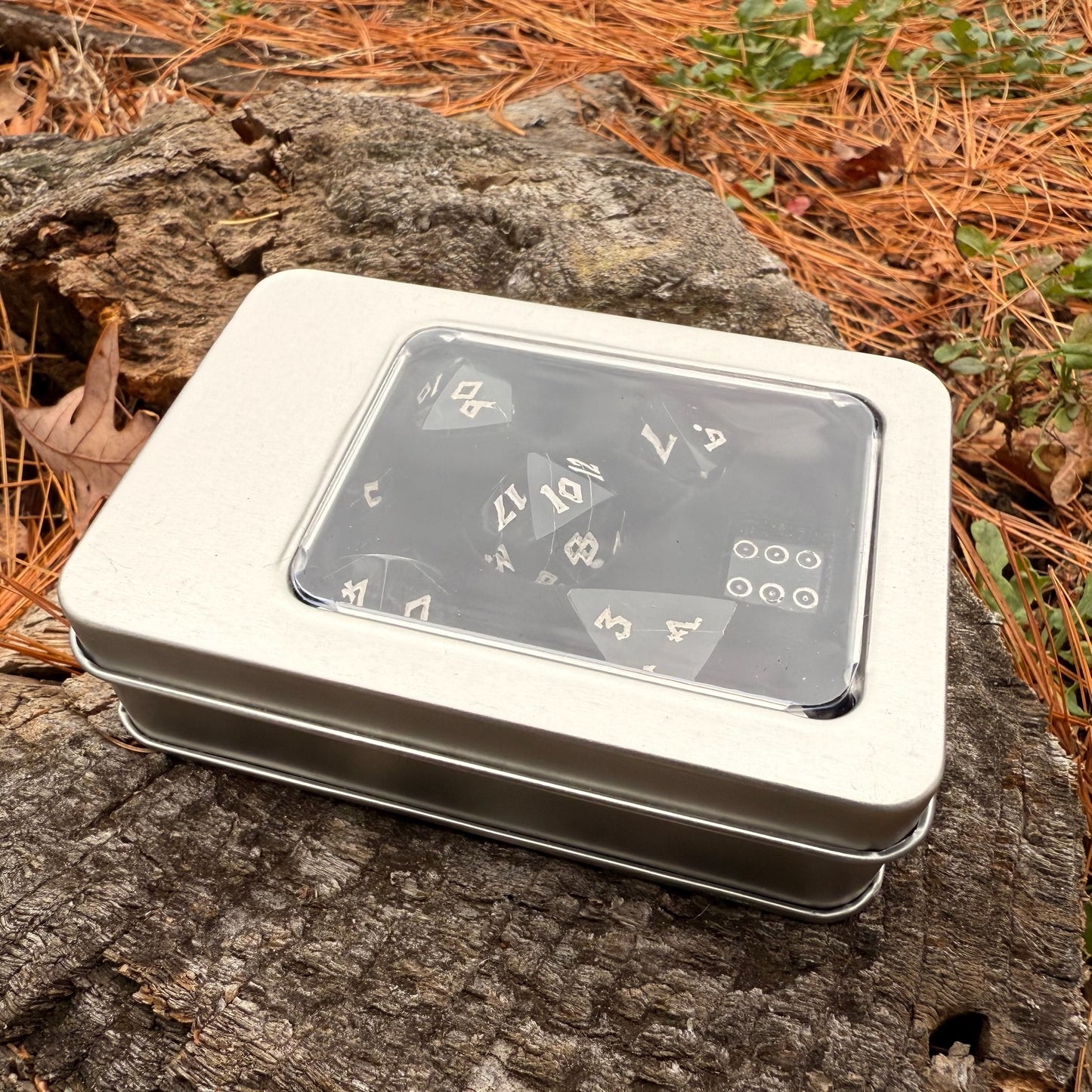 Metallic dice box with polyhedral dice inside on a wooden surface