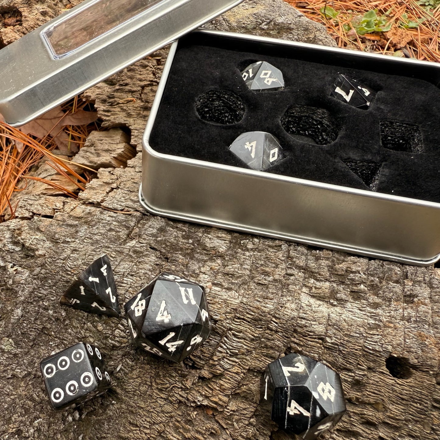 Black polyhedral horn dice with white numbers in a metal dice box on a wooden background.