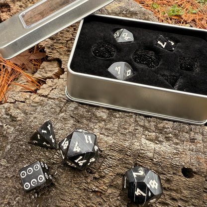Black polyhedral horn dice with white numbers in a metal dice box on a wooden background.