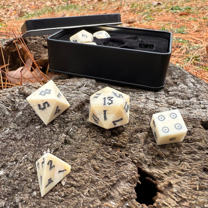 Set of polyhedral bone dice with a black box on a wooden surface outdoors.