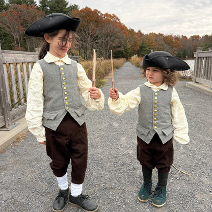 Two children in colonial-style clothing holding wooden toy knives outdoors.