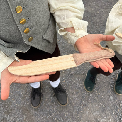 Children holding wooden toy knives outdoors.