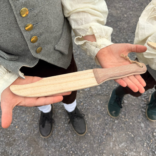 Children holding wooden toy knives outdoors.
