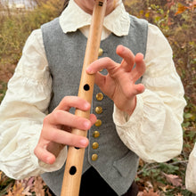 Child playing a bamboo penny whistle outdoors with a natural background