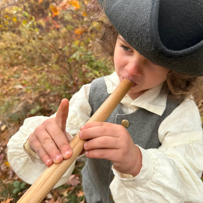 Child playing a bamboo penny whistle outdoors with a blurred natural background