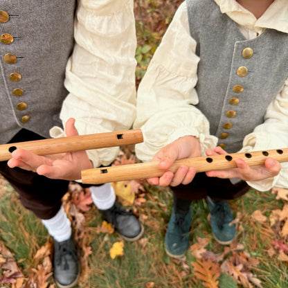 Two children holding bamboo penny whistles outdoors with a natural background