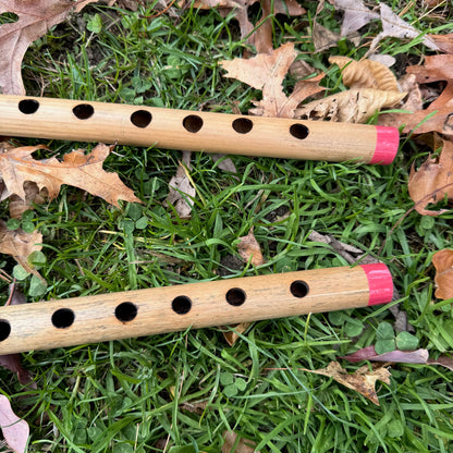 Two bamboo penny whistles with red tips on grass and leaves