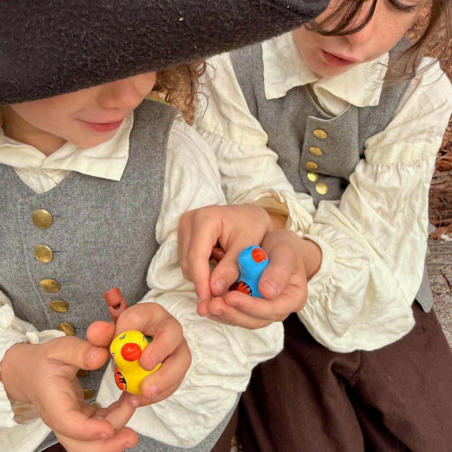 Two children in historical clothing playing with bird whistles.