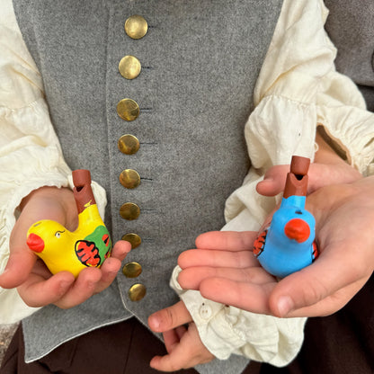 Two children wearing historical clothing holding colorful bird whistles.