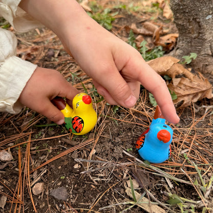 Child's hands playing with colorful bird whistles on the ground