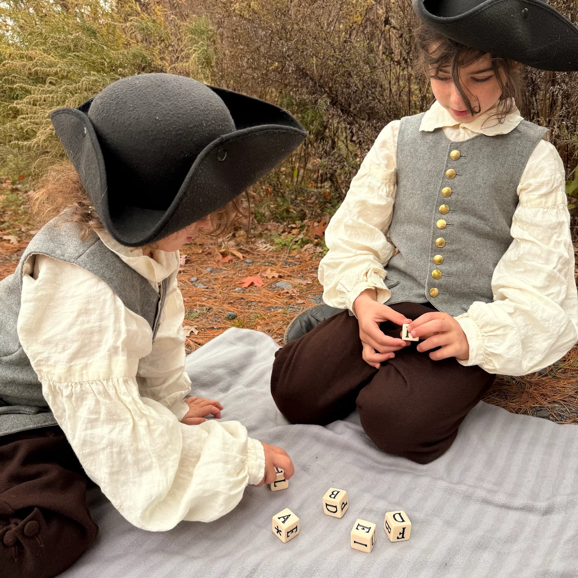 Two children in colonial attire playing with dice outdoors.