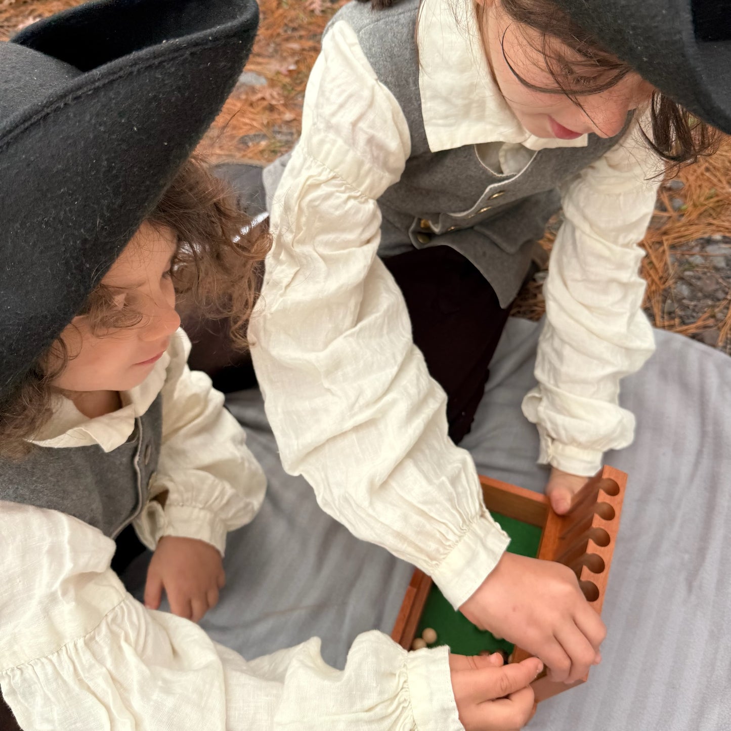 Two children in colonial attire playing with a Captain's Mistress game.