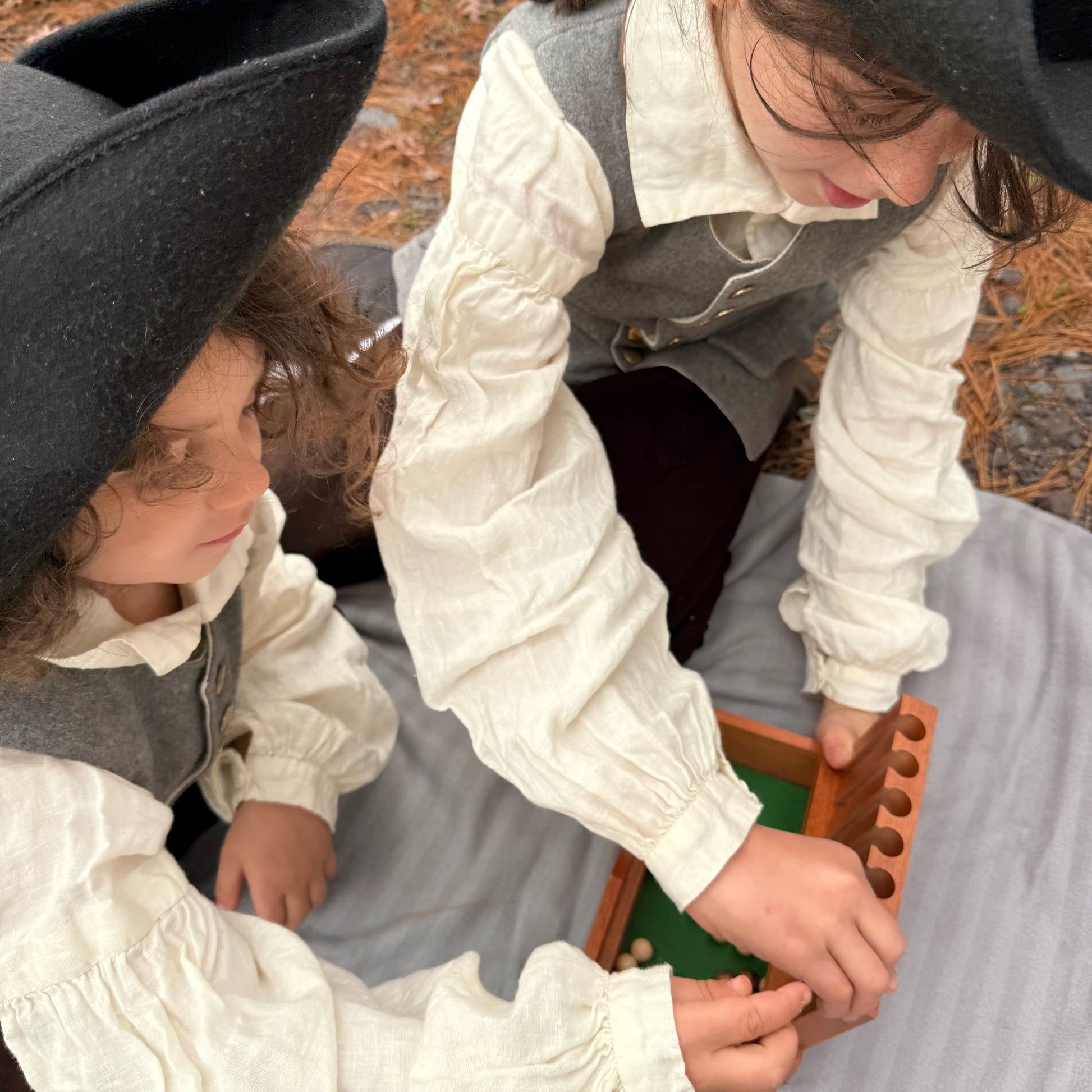 Two children in colonial attire playing with a Captain's Mistress game.