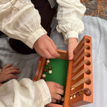 Two children playing with a wooden Captain's Mistress game on a blanket outdoors.