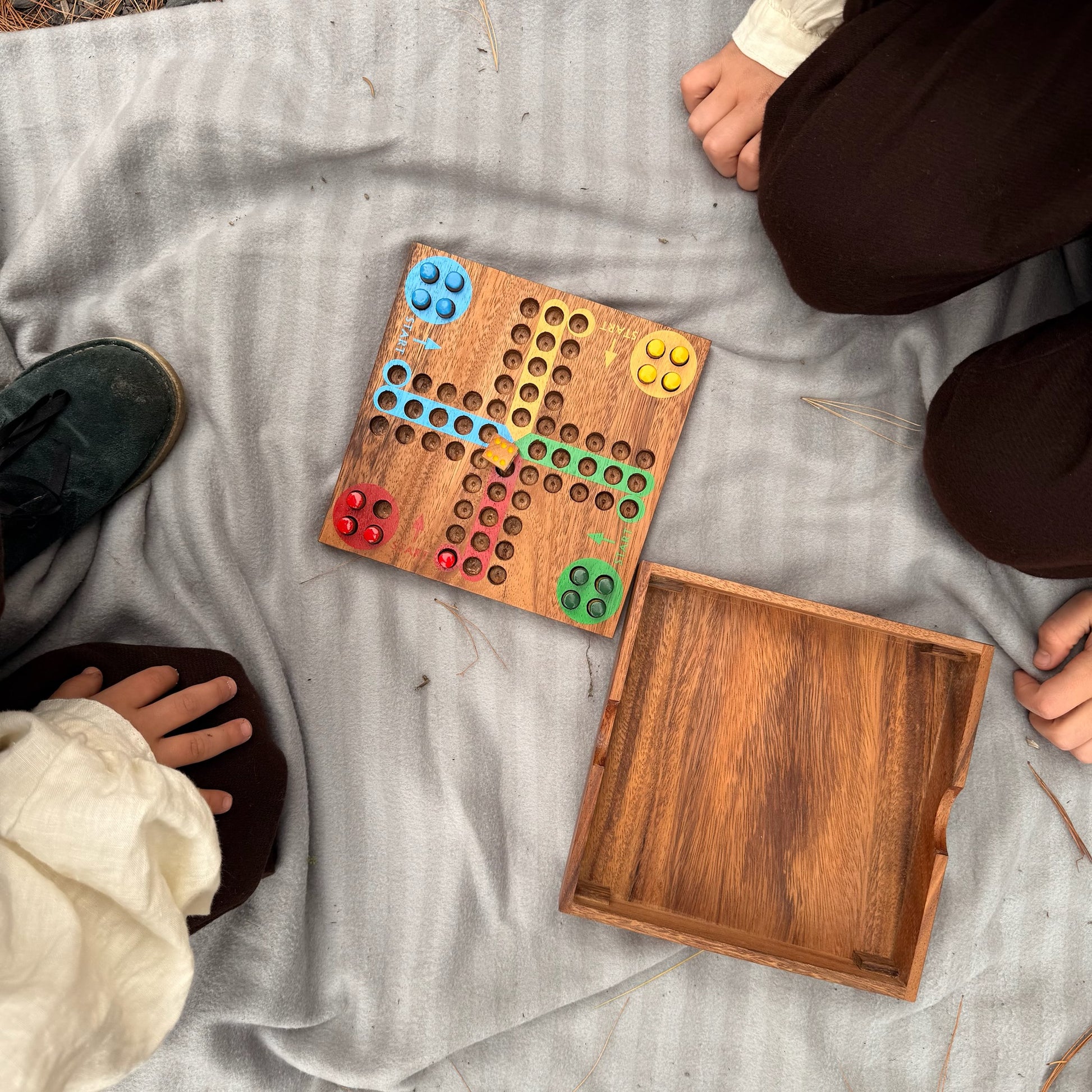 Wooden Ludo board game with colorful pieces on a gray blanket