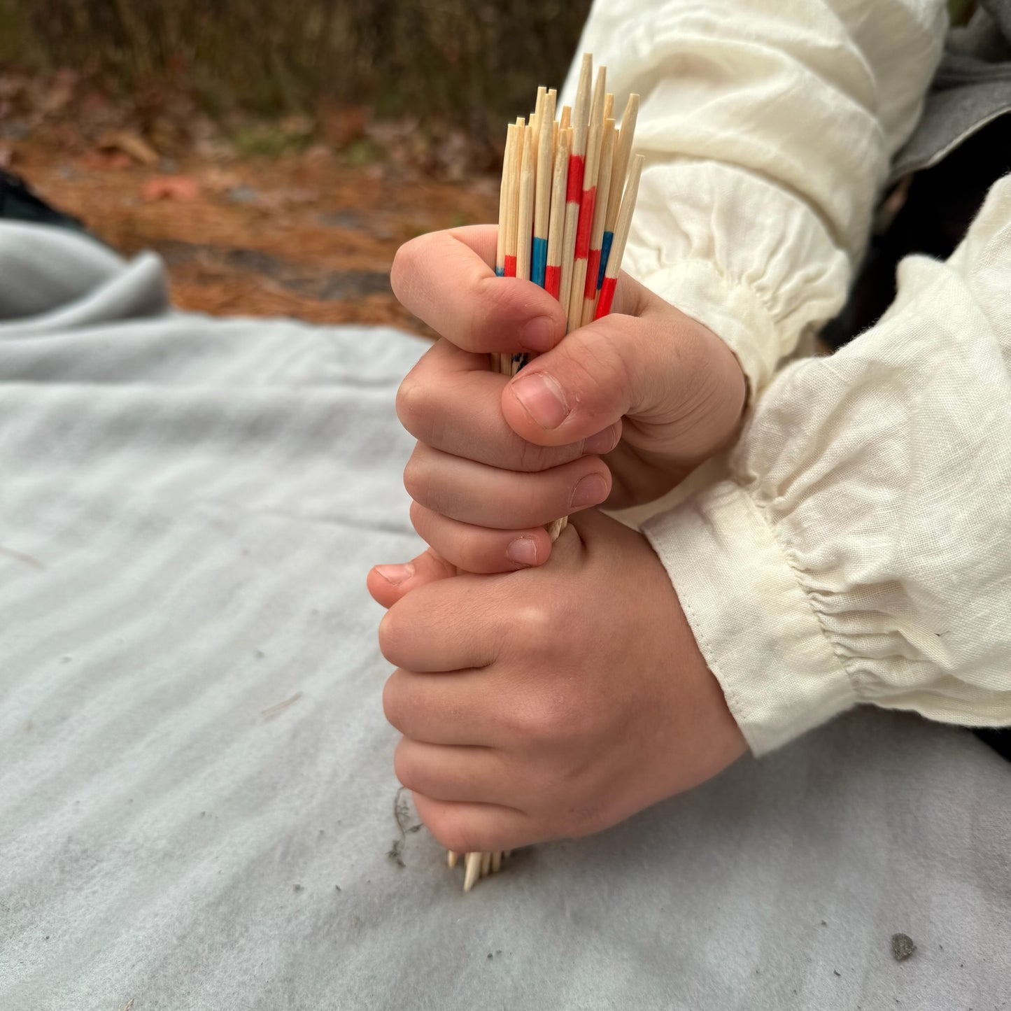 Hands holding a bundle of Pick Up Sticks with colored markings on a natural background