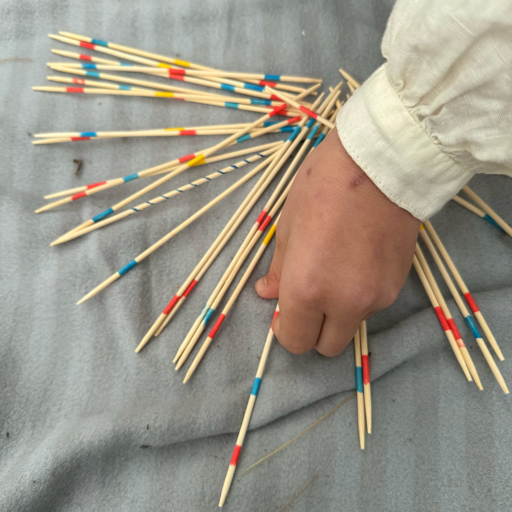 Hands playing with a bundle of wooden Pick Up Sticks with colorful markings on a gray surface