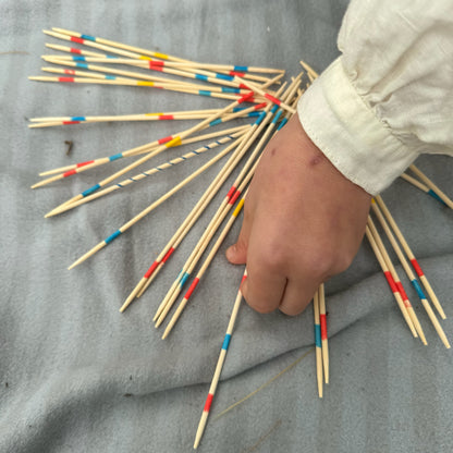Hands playing with a bundle of wooden Pick Up Sticks with colorful markings on a gray surface