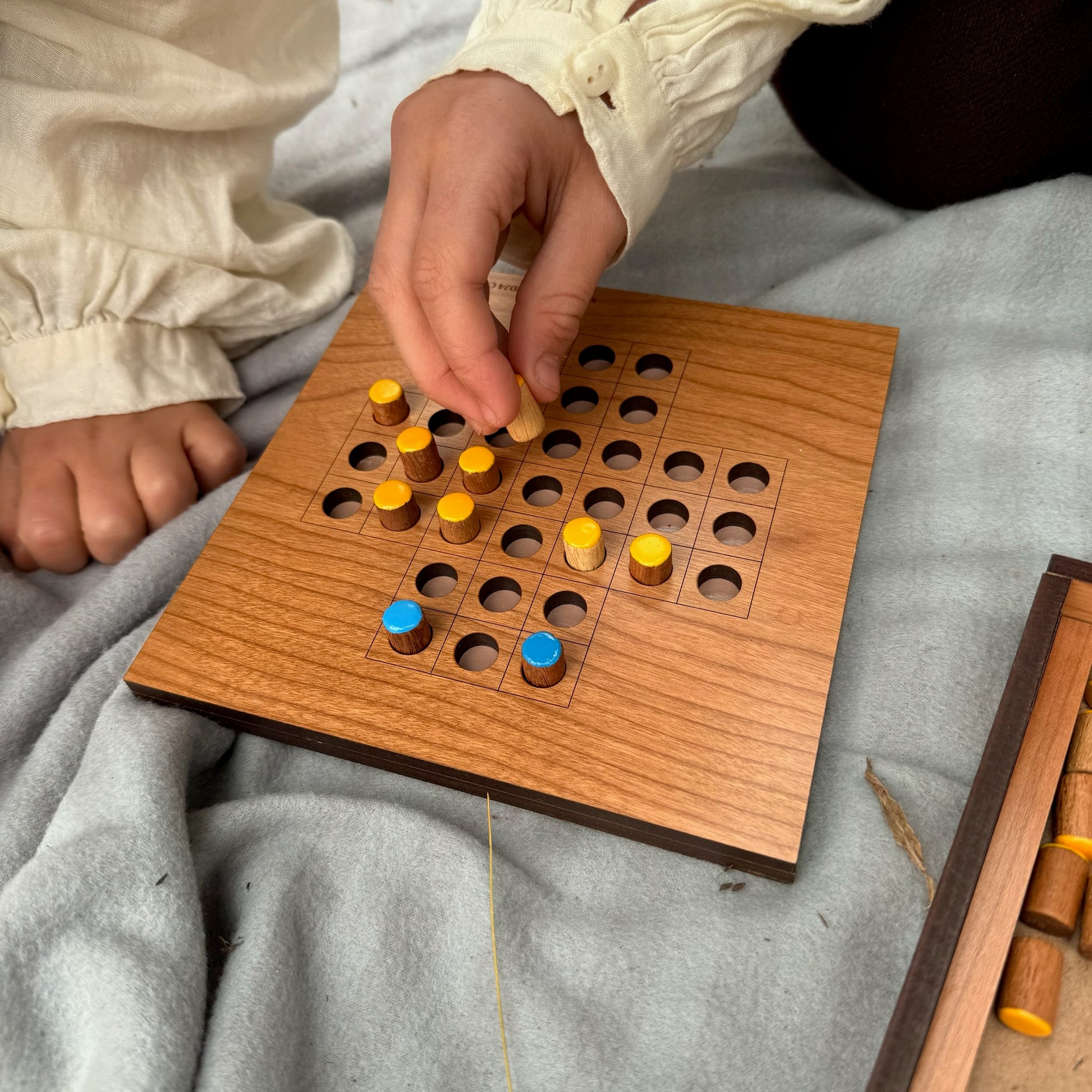 Child playing Solitaire with yellow and blue pieces on a natural background