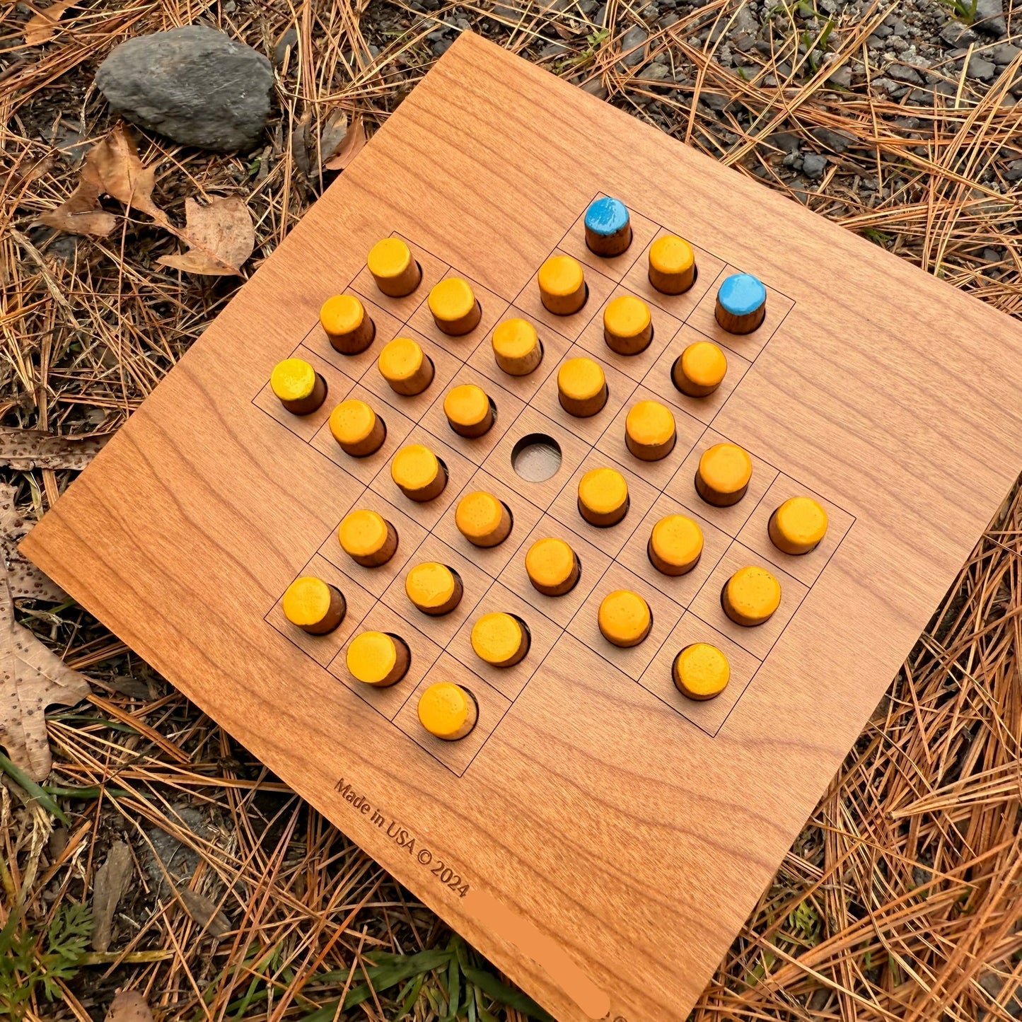 Wooden Solitaire game board with yellow and blue pieces on a natural background