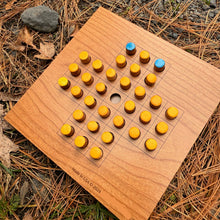 Wooden Solitaire game board with yellow and blue pieces on a natural background