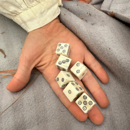 Hand holding six bone dice with black dots on a gray surface
