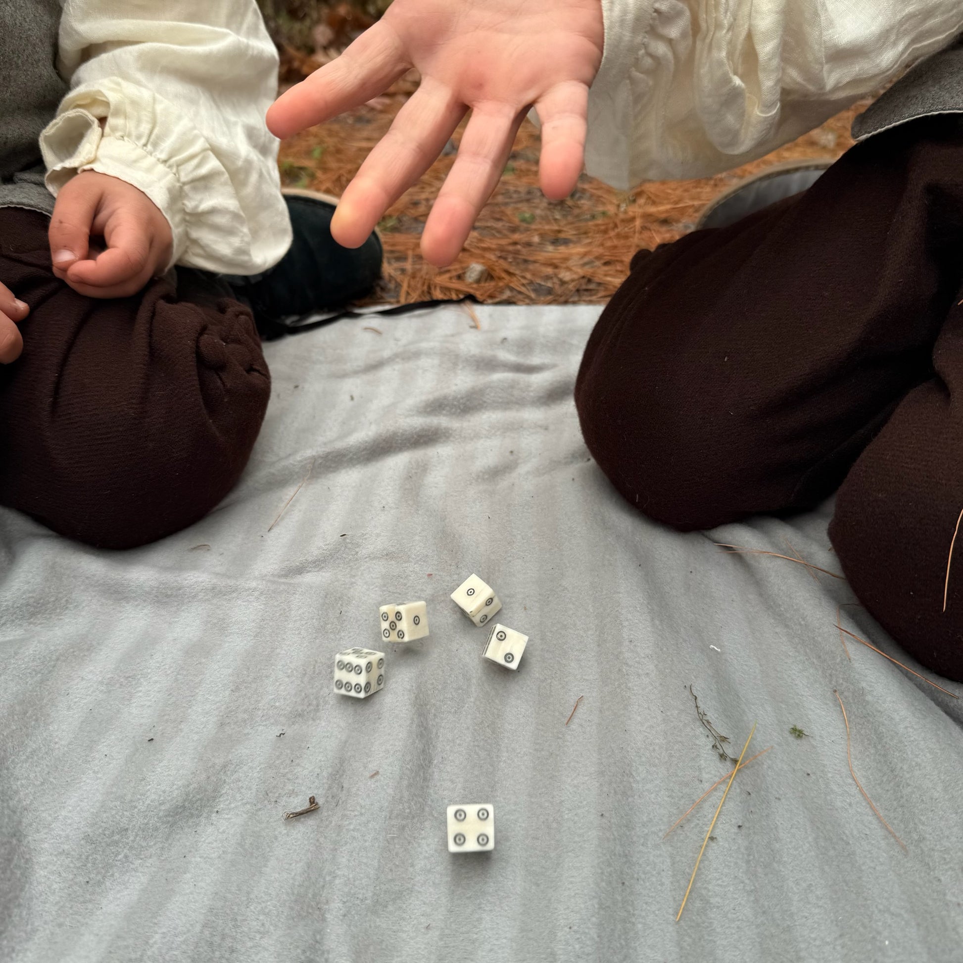 Two children playing with bone dice on a blanket outdoors
