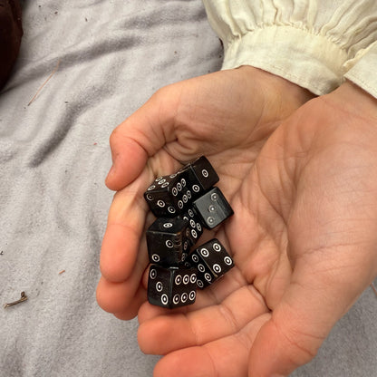 Hands holding black horn dice with white dots on a neutral background