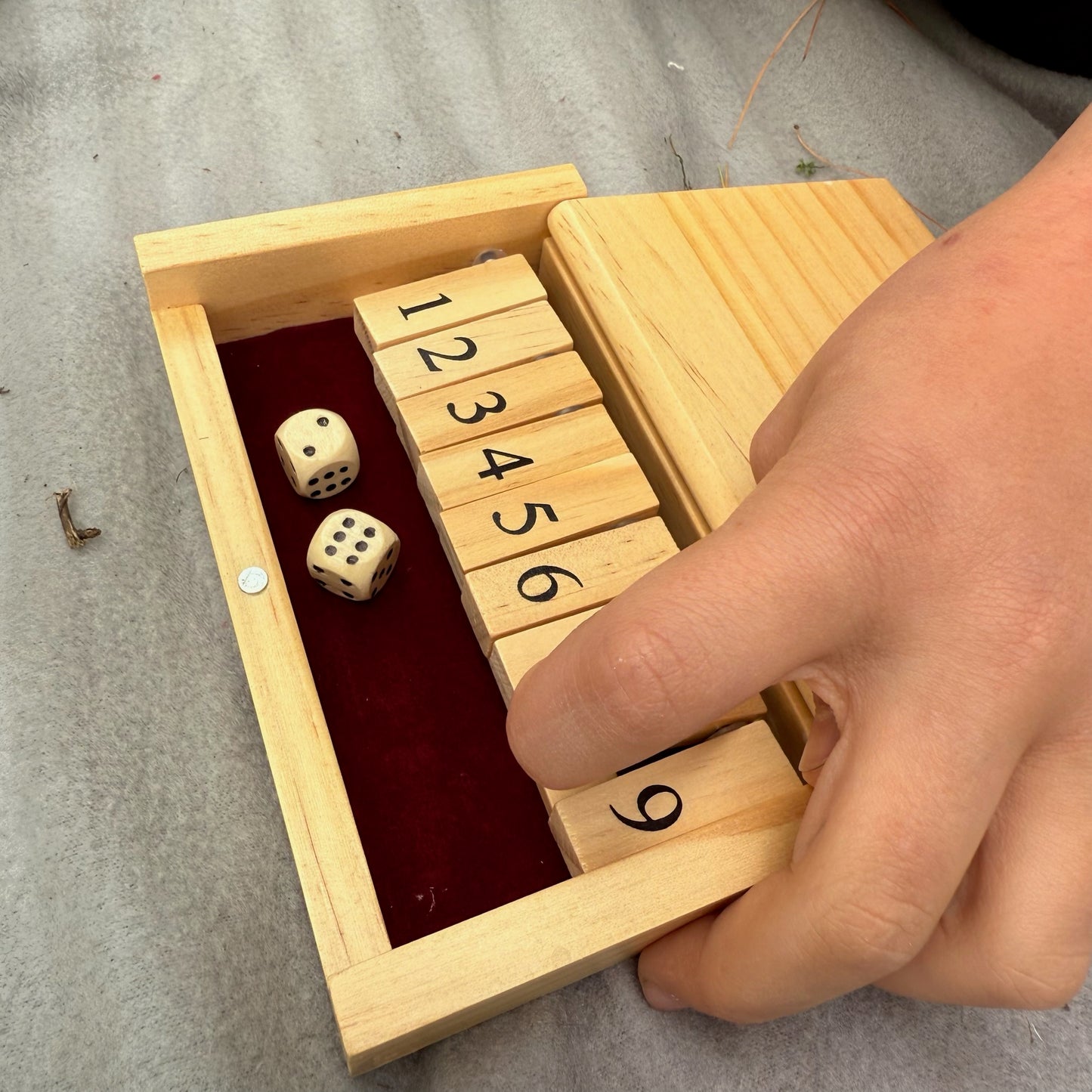 Child playing miniature wooden Shut the Box game on a gray surface