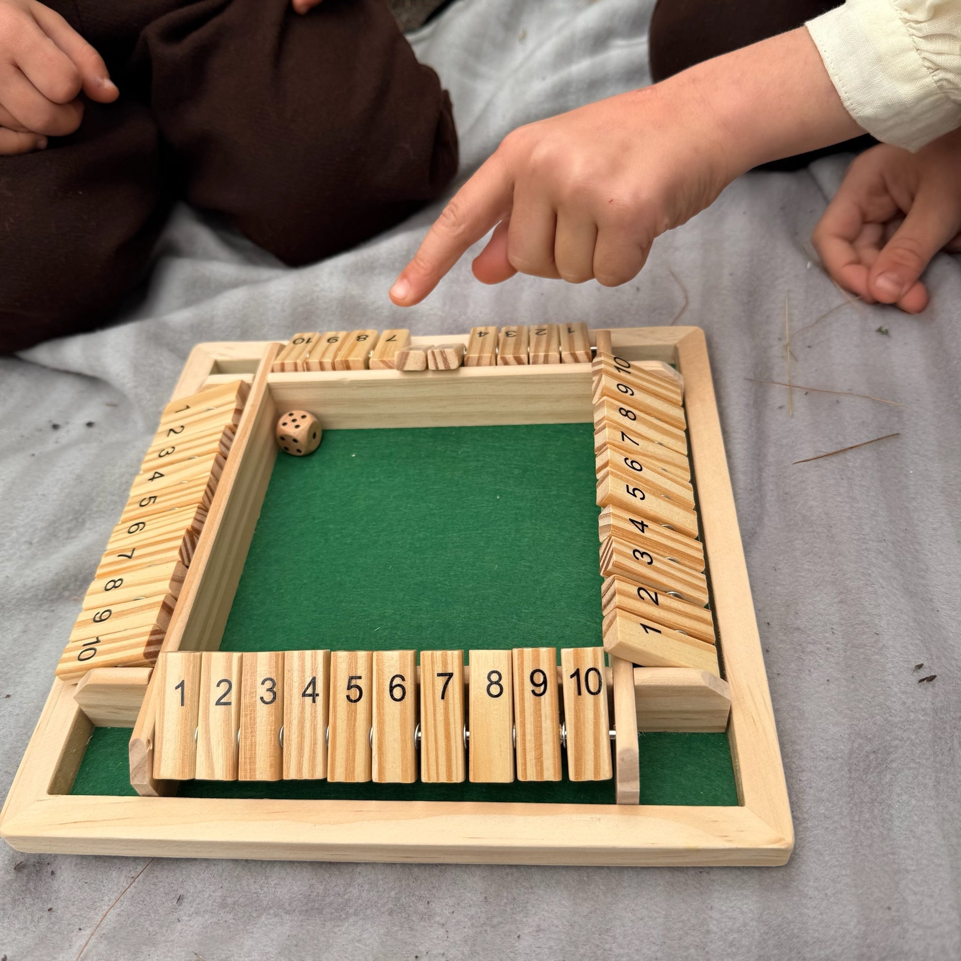Children playing Shut the Box game on a gray surface